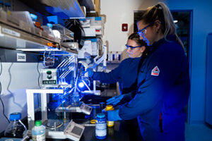 Two Northeastern bioengineering students wearing blue lab coats working in a lab. 