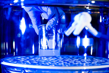 Gloved hands placing a 150mL beaker into a round and clear instrument. 