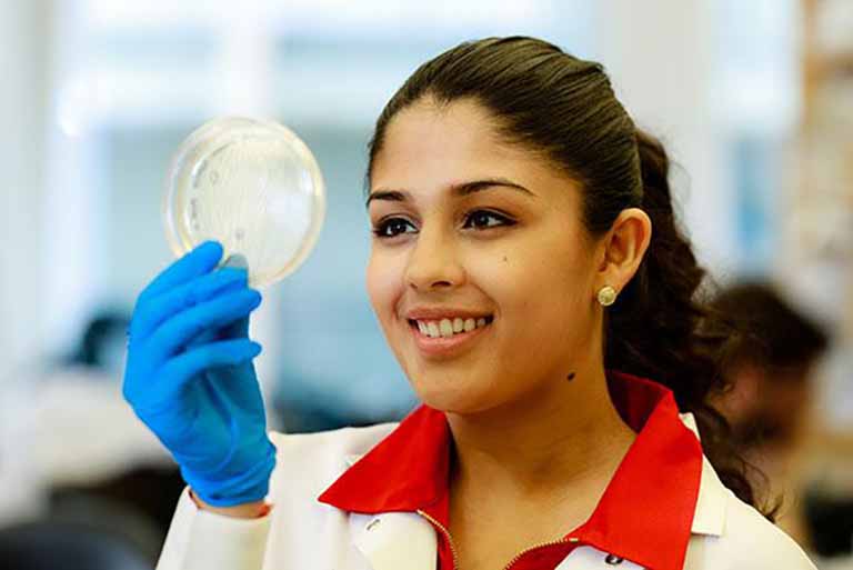 student in lab coat hold petrie dish in lab