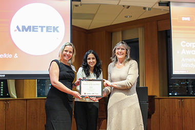 three people standing next to each other with the person in the center holding an award